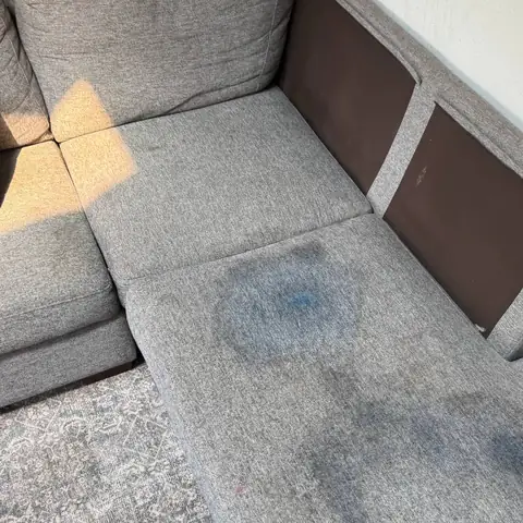 Gray sectional chaise with large dark stains before cleaning